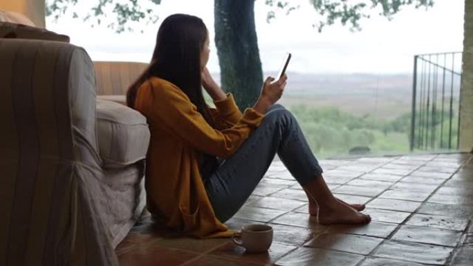 DS年轻女子在托斯卡纳的一所房子的露台上使用智能手机