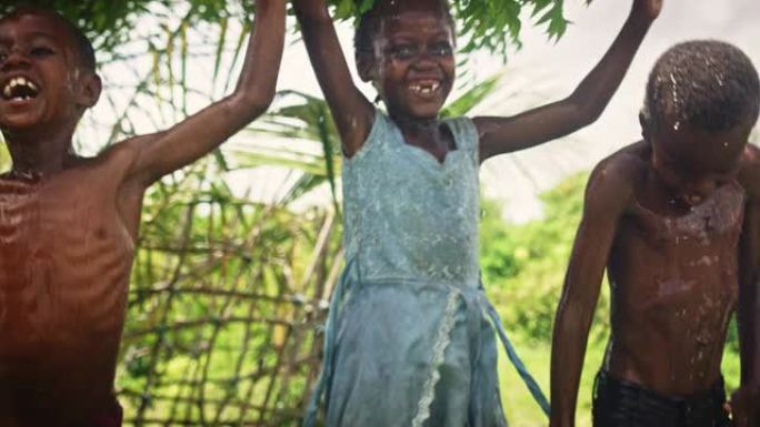 一群非洲孩子在被泼水时又跳又笑。快乐而天真的黑人孩子在长时间干旱后玩耍和享受雨水的祝福。锅里拍摄