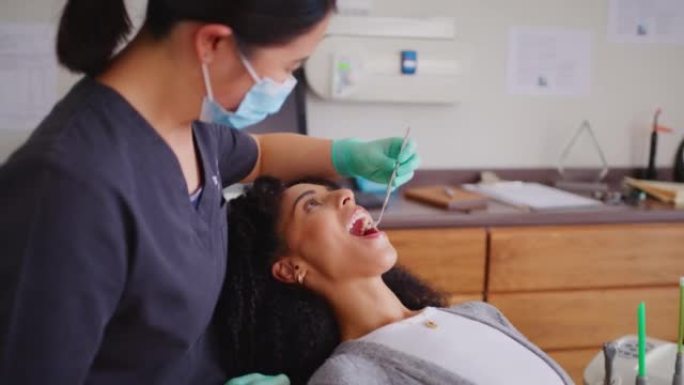 牙医在牙科预约期间用镜子工具检查女性患者的牙齿。非洲妇女进行例行检查，以防止龋齿和牙龈疾病，并保持良