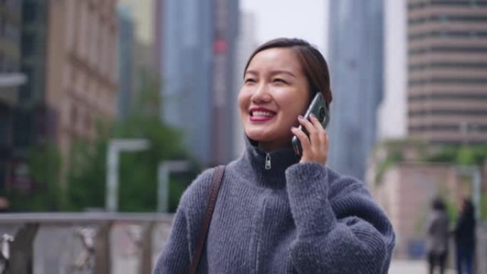 在城市里散步的亚洲妇女通过电话交谈