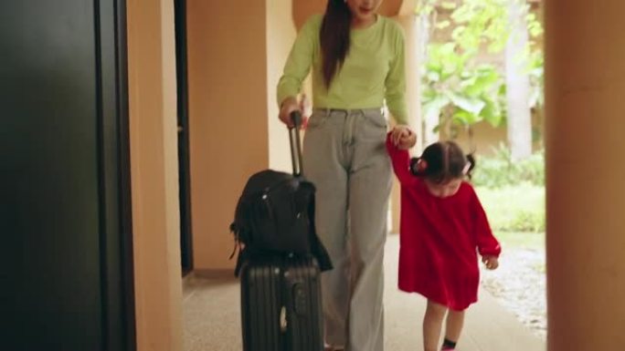 亚洲妈妈边走边牵着女儿的手，边提旅行包。