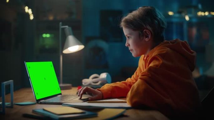聪明的小男孩在绿屏显示的笔记本电脑上研究作业。快乐的青少年浏览教育研究，在笔记本上写作，学习学校材料