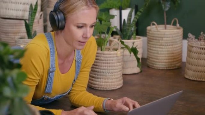 女人使用笔记本电脑，并通过在花店工作的无线蓝牙耳机在线听音乐。植物学家在互联网上搜索植物研究并在工作