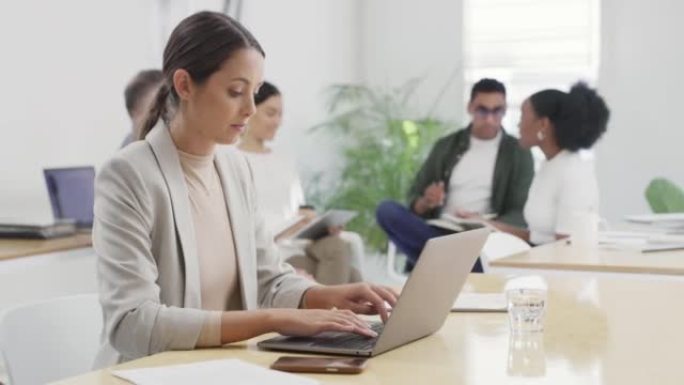 女商人在繁忙的办公室里用笔记本电脑工作，同事在后台。专注的企业家浏览互联网，同时在创业公司的办公桌或