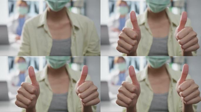 自信的亚洲女医生戴着防护口罩，年轻的病人女孩在诊所或医院的办公桌上做着竖起大拇指微笑。