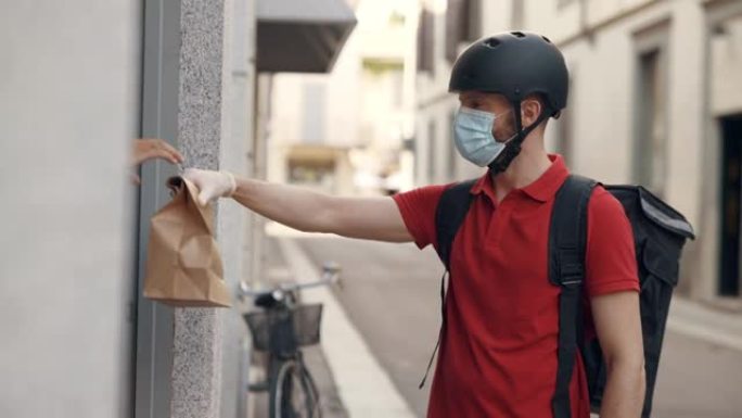 一位戴着防护口罩和手套的年轻快递员正在安全地向客户提供带有新鲜食品的杂货订单。快递、送货上门、电子商