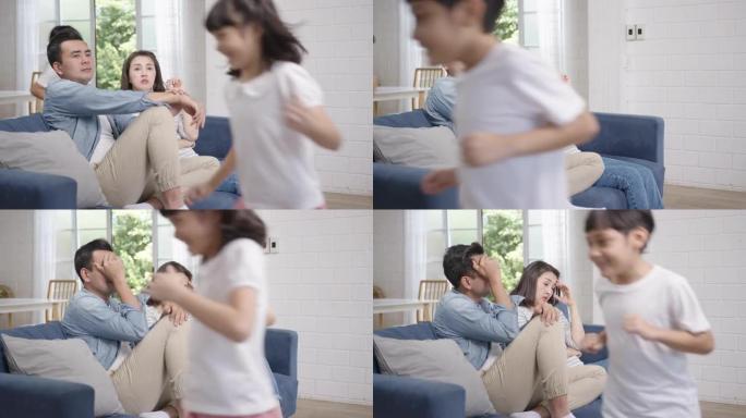 亚洲家庭父母坐在沙发上感到无聊，烦恼和疲惫。女儿和儿子在家里的客厅沙发上大喊大叫。电晕病毒预防检疫。