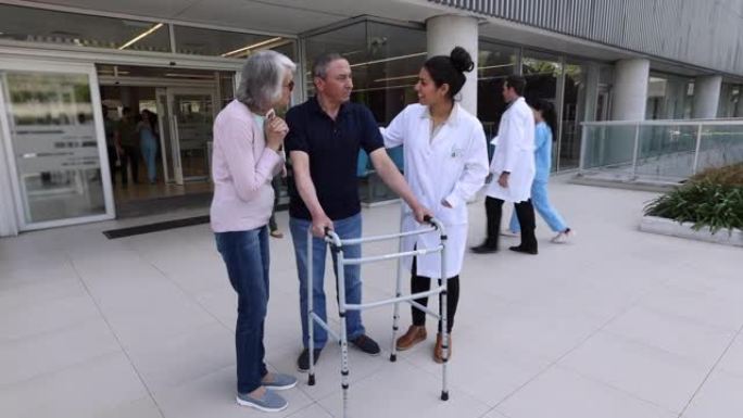 女医生在医院外使用助行器和他的妻子与男性患者交谈