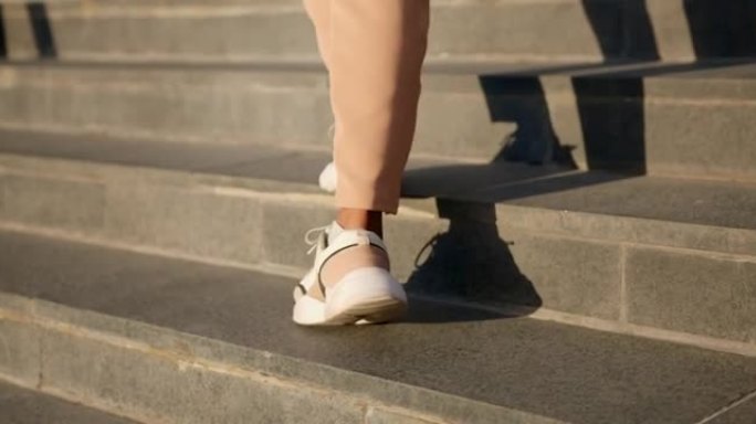 穿着现代运动鞋的年轻女子的脚在阳光下跳上楼梯