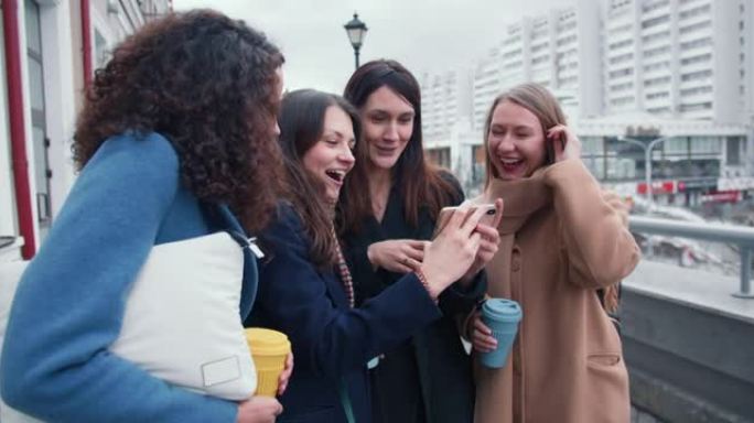 一群年轻快乐美丽多样的女性朋友在阴天秋日在城市街道的智能手机上观看视频。