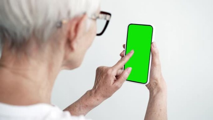 老人触摸屏智能手机，带绿色色度键特写。60多岁的女性手持手机点击模型。概念观看和展示互联网社交媒体，