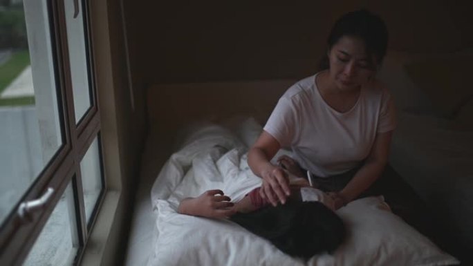亚裔华裔妈妈在床上照顾女儿，用温度计测量体温