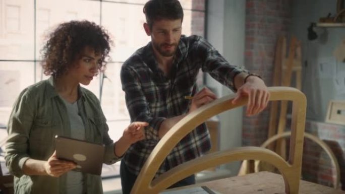 两个小企业主使用平板电脑的肖像，并在家具车间讨论新木椅的设计。木匠和一个在阁楼工作室工作的年轻女学徒