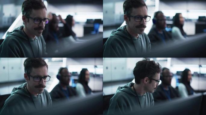 一位快乐的大胡子计算机科学团队成员在研发技术中心设施的计算机上工作的肖像。微笑的男人为工业软件编写代