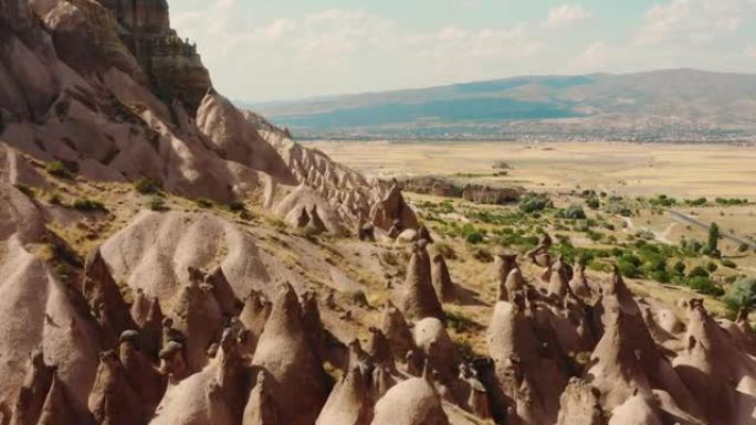 无人驾驶飞机在阳光明媚的山崖一侧独特的岩石上方飞行，卡帕多西亚美丽的电影立交桥景色。