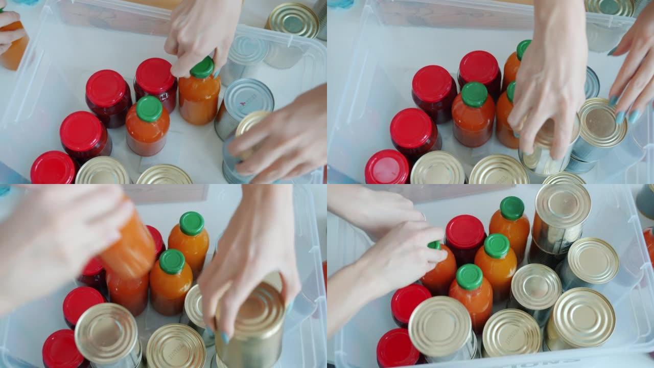 志愿者的手的高角度视图将食物提供罐装蜜饯和果汁瓶放入捐赠盒中