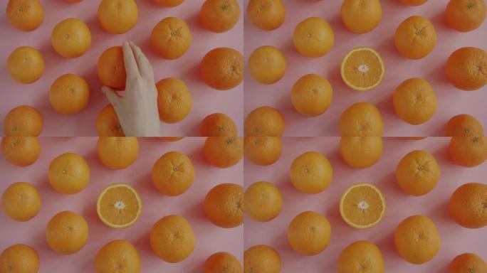 放大粉红色背景上美丽成熟的橘子和女性手拿走一半的水果