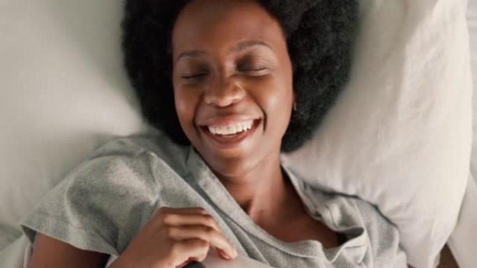 女孩躺在床上，智能手机在社交媒体应用程序上带着微笑阅读有趣的消息。早上在卧室里快乐的黑人妇女，通过手