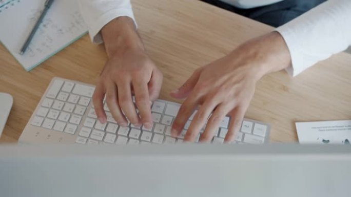 在办公桌室内用电脑键盘打字的男性手的高角度视图特写