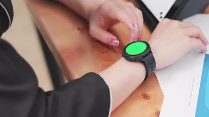 年轻的商务女性在工作中触摸绿屏背景的智能手表