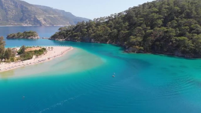 人们在蔚蓝的海湾岸边的沙滩上享受日光浴。土耳其奥鲁德尼兹附近海湾地中海蔚蓝水的鸟瞰图。船驶过最纯净的
