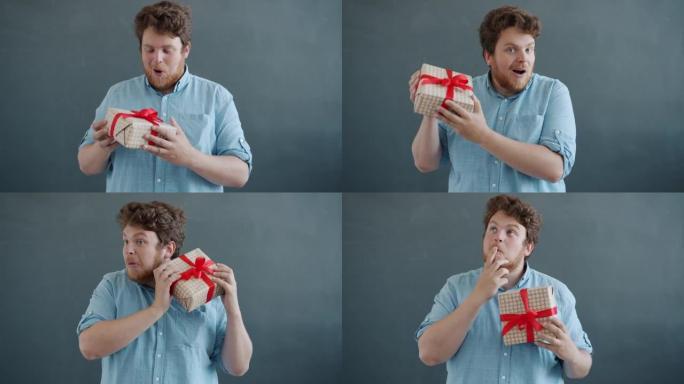快乐的家伙拿着生日礼物摇晃礼品盒的肖像带着幸福和快乐看着相机