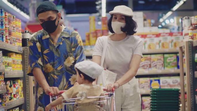 年轻的家庭带着戴着口罩的小女孩在超市购物