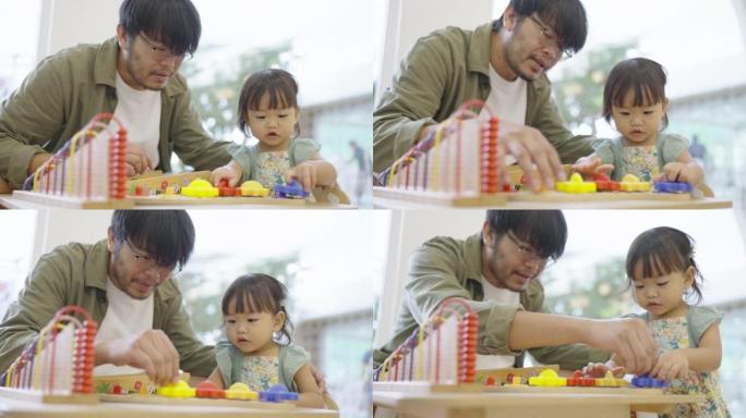 亚洲父亲协助他的小女孩在桌子上玩玩具。