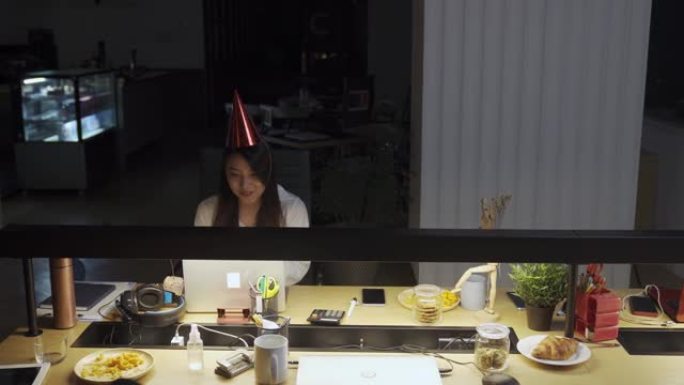 亚洲华裔美女独自在办公室工作到很晚，与她在其他分支机构的同事庆祝生日视频会议