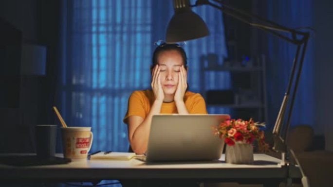 深夜工作的亚洲妇女在现代家庭的客厅用笔记本电脑感到压力