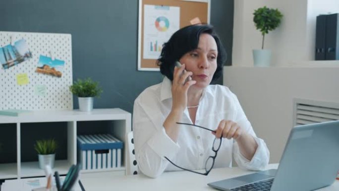 女企业家在手机上讨论业务并在现代办公室中使用笔记本电脑