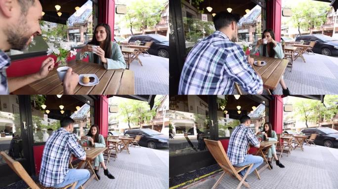 快乐的女人在与坐在咖啡馆外面的平板电脑上的伴侣交谈时享受咖啡