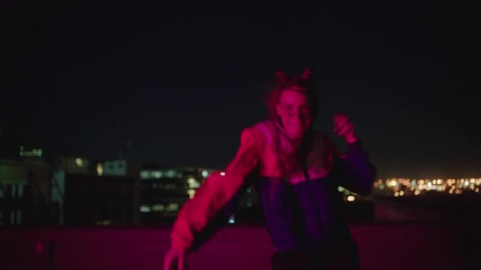 快乐的女人晚上在屋顶上跳舞，庆祝享受愚蠢的舞蹈，享受快乐的舞蹈女孩在城市里带着红灯