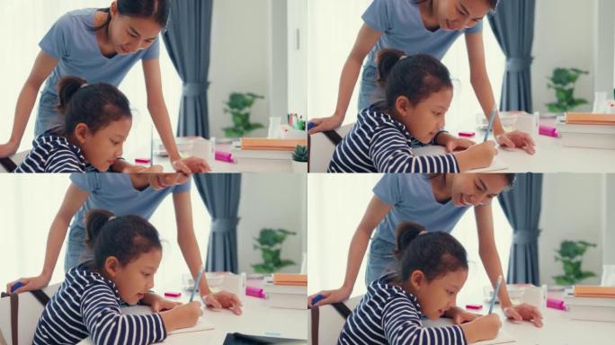 穿着毛衣的亚洲蹒跚学步的女孩坐在桌子前，拿着记事本，用铅笔专注于写笔记本，周末在家和妈妈或家教做数学