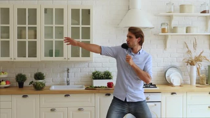 英俊快乐的男人独自在现代厨房唱歌跳舞