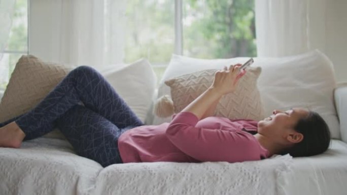 亚洲妇女躺在沙发上使用智能手机