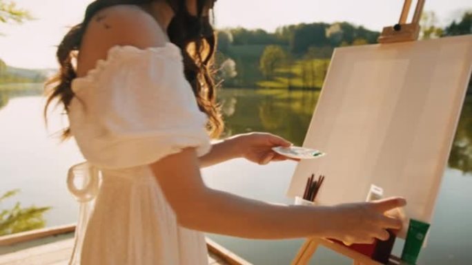 女艺术家站在湖上的码头上时，将颜料管挤到调色板上