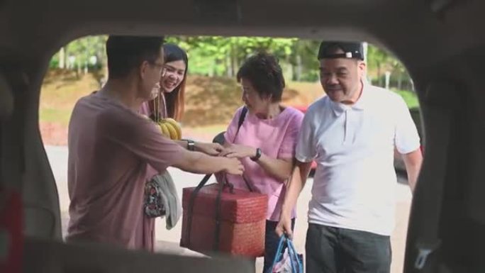 亚洲中国多代家庭从MPV汽车后备箱中卸下篮子中的食物和饮料，准备在停车场野餐