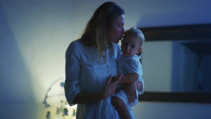 真实的电影拍摄的年轻和平的新妈妈在晚上在托儿所睡觉前抱着新生婴儿