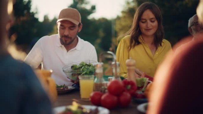 一个英俊的大胡子男人在花园餐桌上放一盘素食沙拉的肖像。幸福的大家庭聚集在一起，在舒适的氛围中举行周末