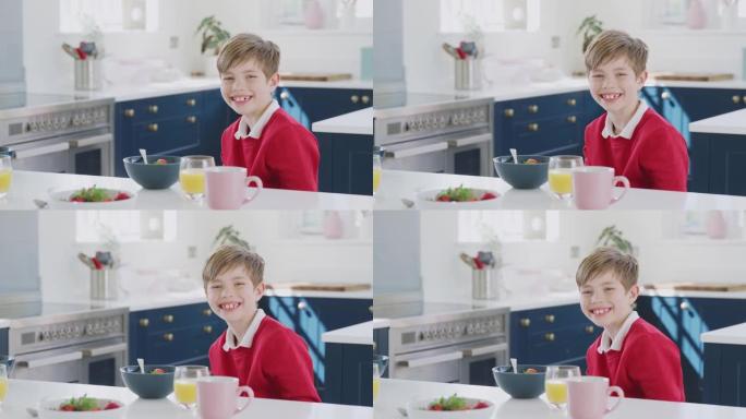 穿着校服的微笑男孩在厨房柜台吃早餐的肖像