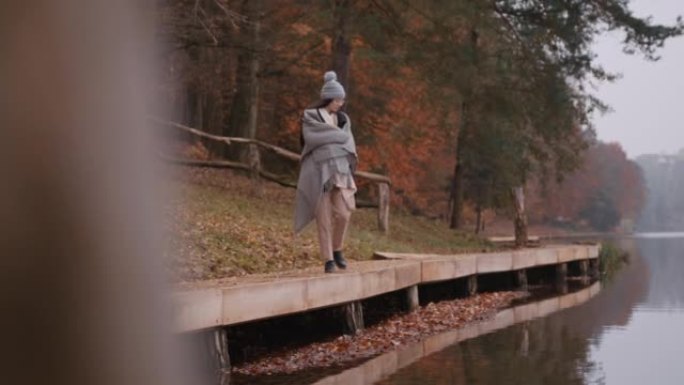 年轻女子在湖上的木板路上行走时用毯子包裹自己