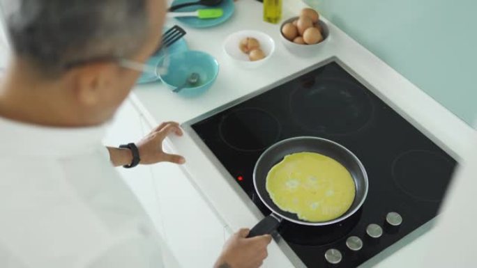 早上准备早餐的高角度亚洲中国高级男子在厨房用烹饪锅煎鸡蛋