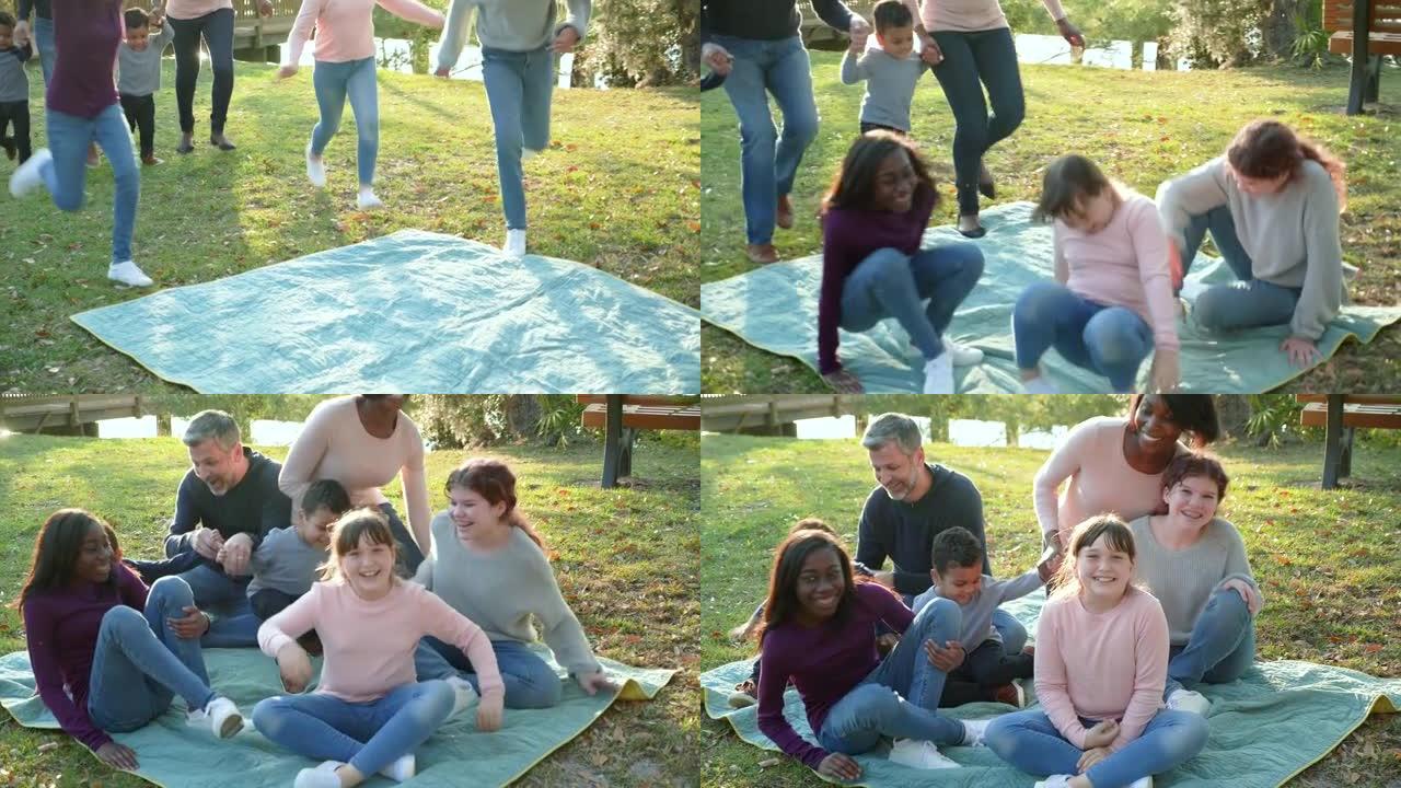 公园里的大型混合家庭，奔跑并坐在毯子上
