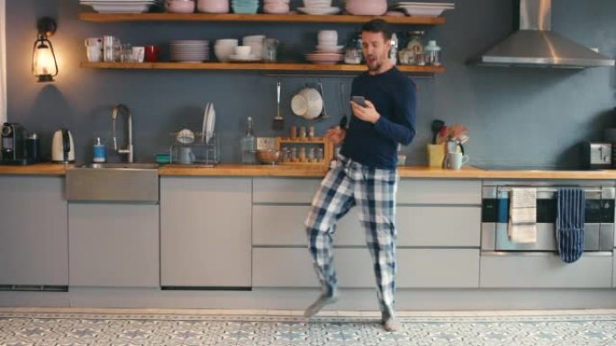 4k视频片段，一个年轻人在家里的厨房里跳舞时使用电话
