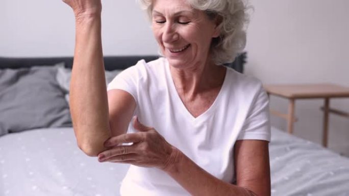 快乐的老年退休妇女用保湿乳液保湿肘部。