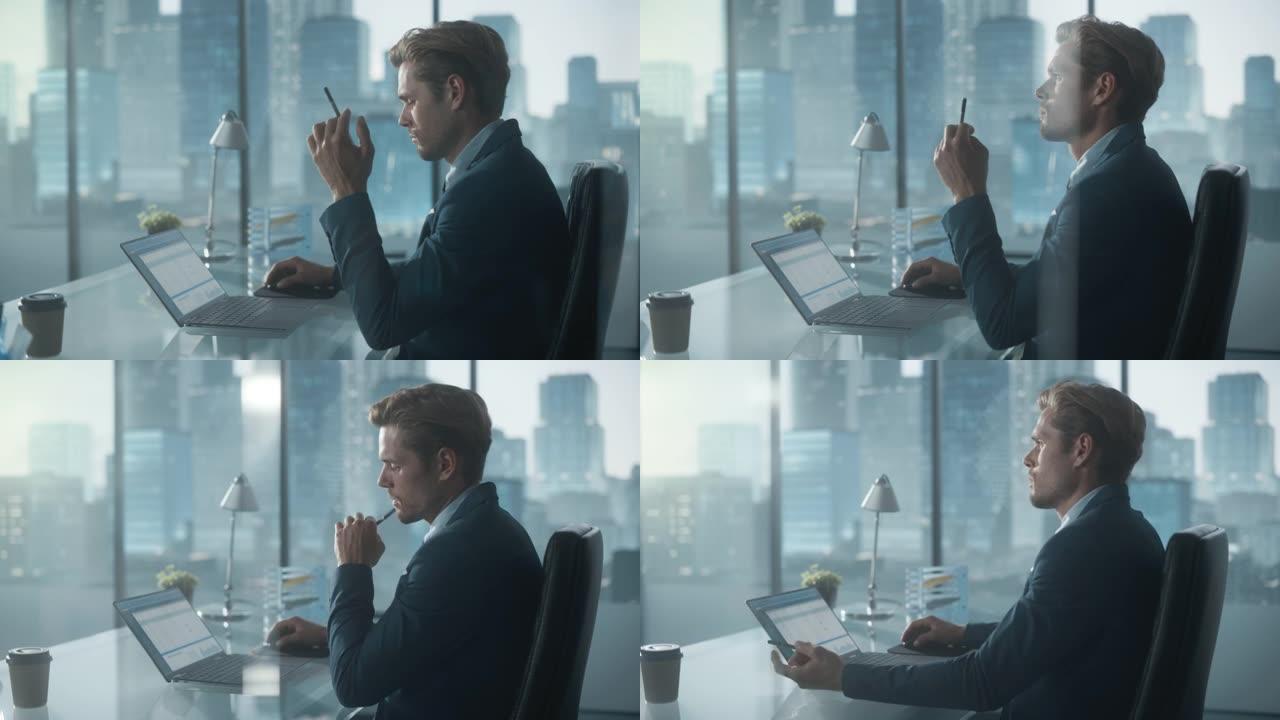 自信的商人穿着西装，坐在现代办公室的办公桌前，使用笔记本电脑，在窗户旁边，可以看到摩天大楼。成功的财