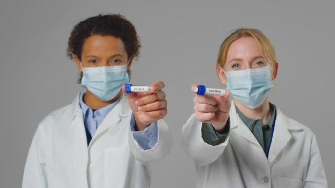 工作室拍摄的实验室研究人员戴着口罩，手里拿着标记为Covid-19和疫苗的试管