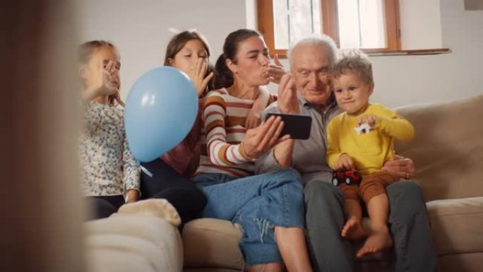 快乐的小家庭在智能手机上进行视频通话，坐在客厅的沙发上挥舞着。通过互联网和技术与远亲建立联系的三代家
