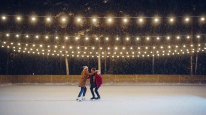 冬季仙境: 滑冰夫妇在一个神奇的夜晚在溜冰场上玩得开心。美丽的雪落下，灯光闪耀。恋爱中的男孩和女友，